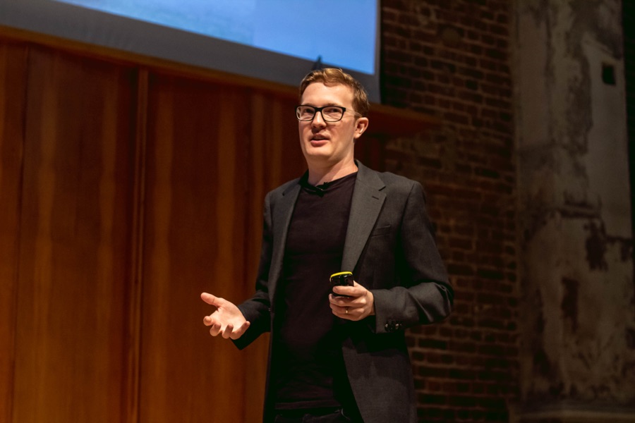 Henry presenting in front of a brick wall and red curtain