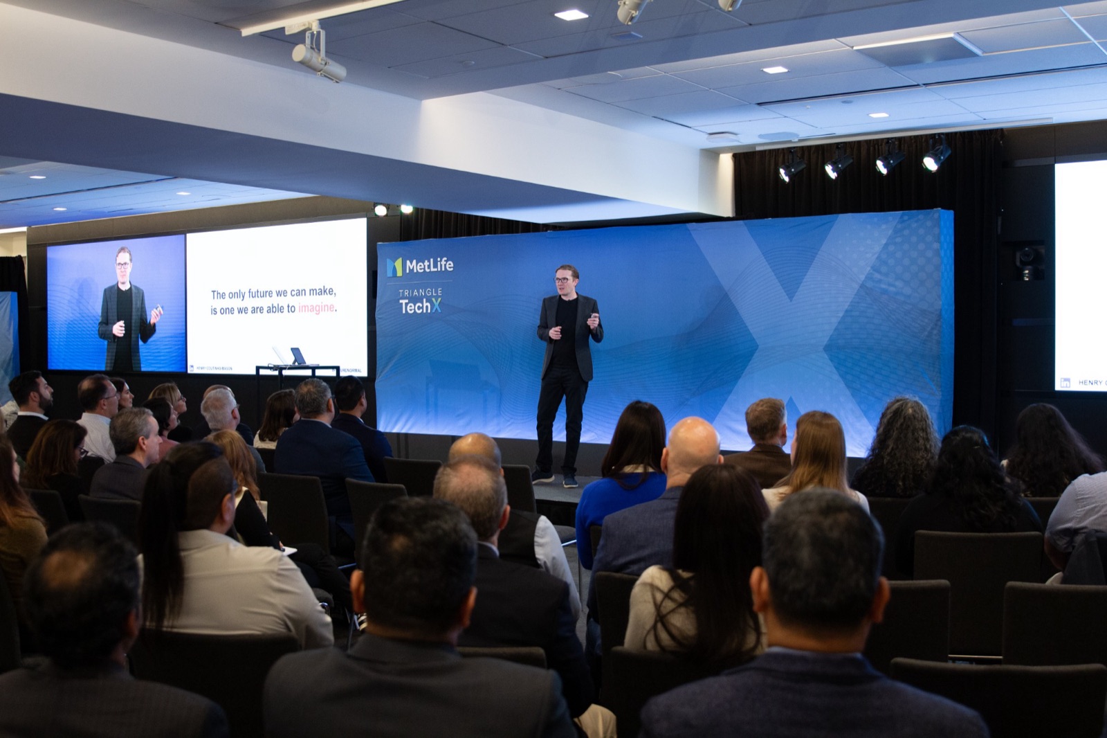 Henry Coutinho-Mason on stage at MetLife Triangle TechX, presenting to a full room